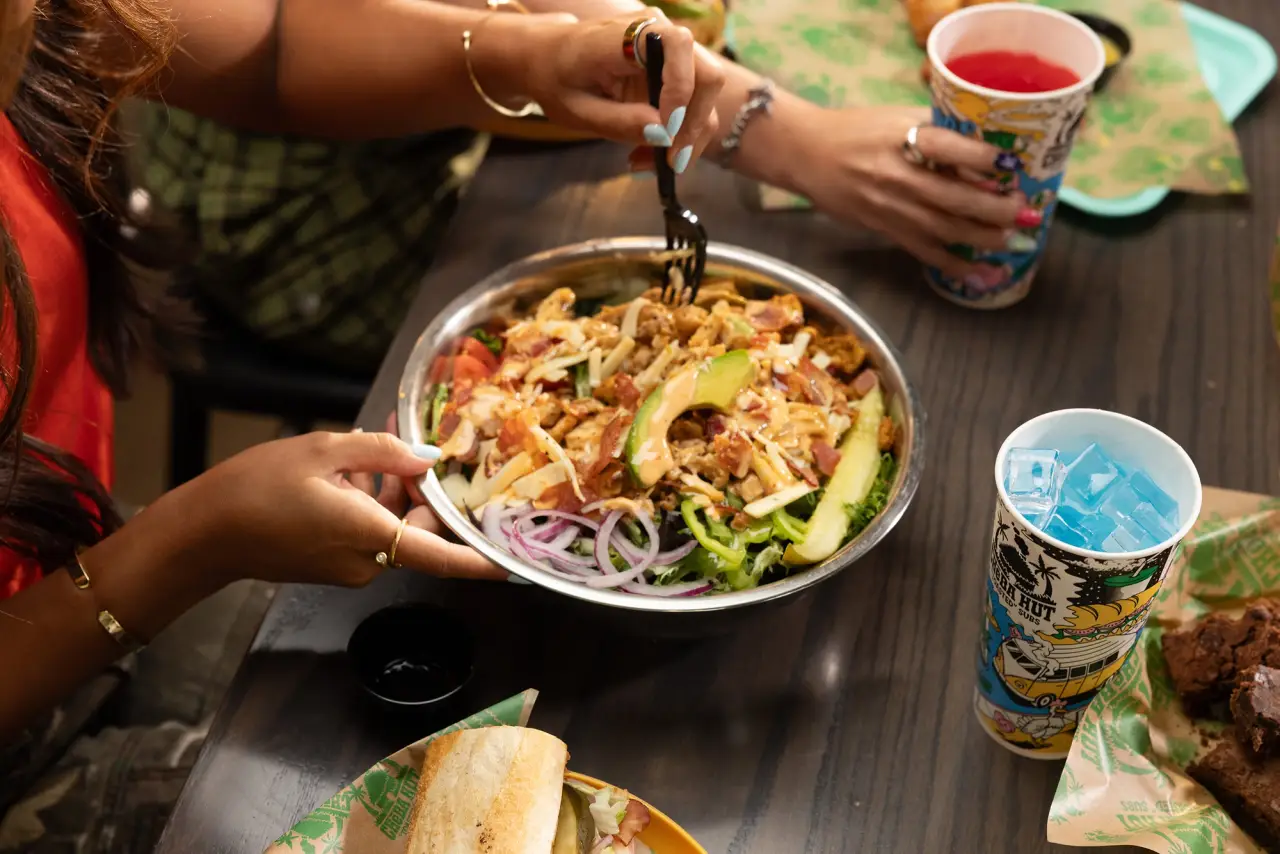 Loaded salad with chicken, bacon, cheese, avocado, and vegetables beside a Cheba Hut drink